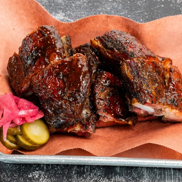 Creekside BBQ ribs with a dark glaze, served with pickled onions and cucumber slices.