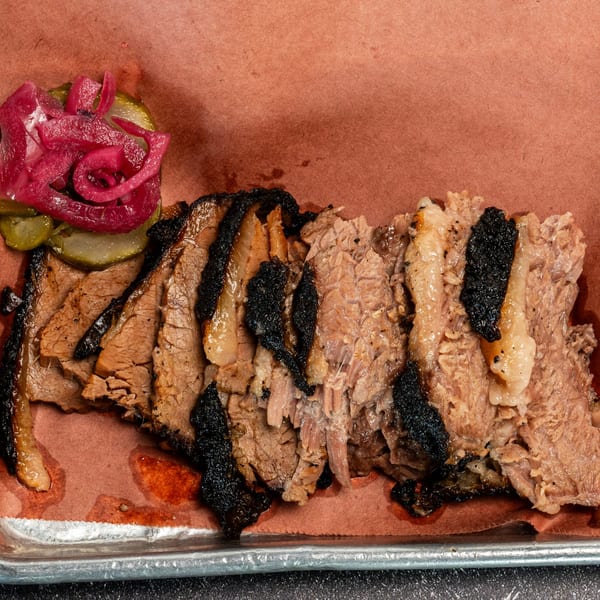 Creekside BBQ brisket slices with charred edges, pickles, and pickled red onions on a tray.