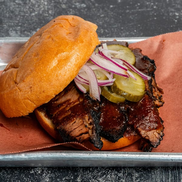 Creekside BBQ brisket sandwich with pickles and red onions on a metal tray.