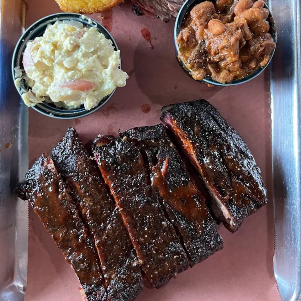 Creekside BBQ ribs with baked beans and potato salad on a metal tray.